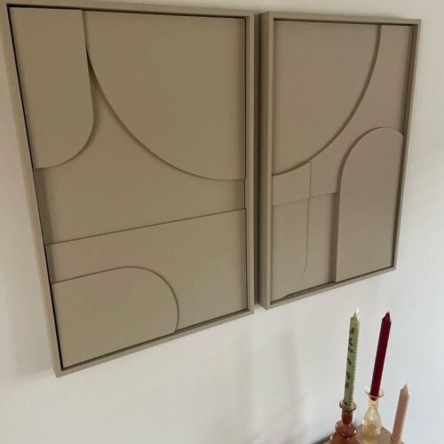 Pack 2 tableaux abstraits 3D faits main moderne en couleur beige, accrochés sur un mur blanc à coté d'un Boujeoir dans un salon.